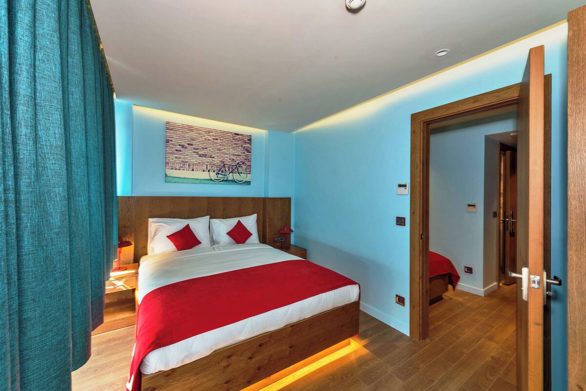 A bedroom with a wooden bed, a nightstand, a wall-mounted painting, and a door leading to another room.