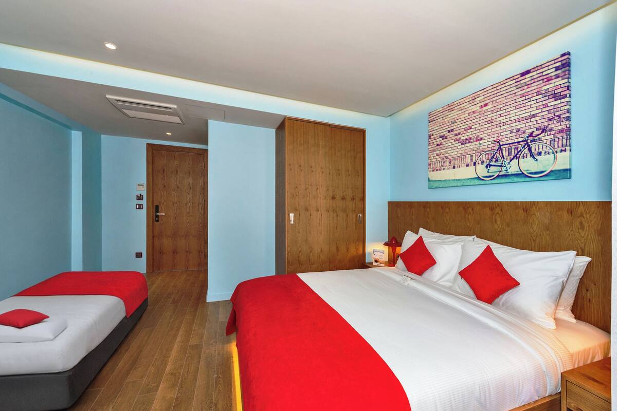 A hotel room with a large bed, a smaller bed, wooden wardrobe, and a wall-mounted artwork of a bicycle.