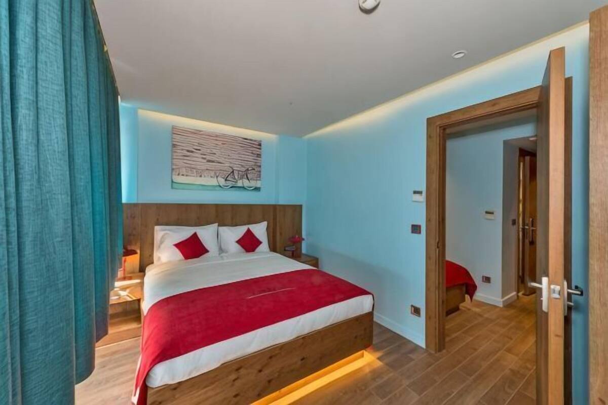 A bedroom with a wooden bed, a red and white bedspread, a nightstand, and a wall-mounted artwork.