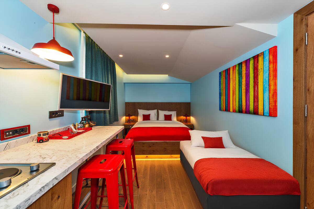 A compact hotel room with a kitchenette, two beds, and a colorful artwork on the wall.