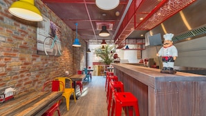 Interior de restaurante con paredes de ladrillo, mesas de madera, sillas rojas y amarillas, y una estatua de chef.