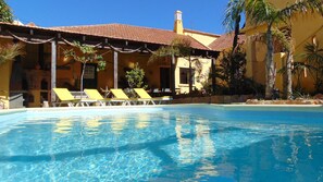 A clear blue pool with yellow lounge chairs and a yellow building with a tiled roof. - Casa Mestre Guesthouse (Vila do Bispo)