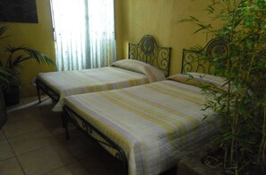 A room with two beds, each with a striped bedspread, a potted plant, and a window with curtains. - Casa Mestre Guesthouse (Vila do Bispo)