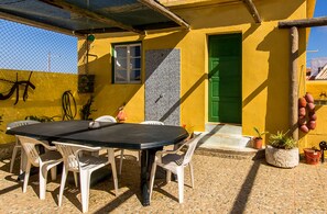 A patio with a table and chairs, a green door, and a tiled wall. - Casa Mestre Guesthouse (Vila do Bispo)
