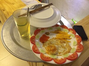 A plate of food with a fried egg, tomato slices, and cucumber, accompanied by a glass of yellow beverage and chopsticks on a tray.