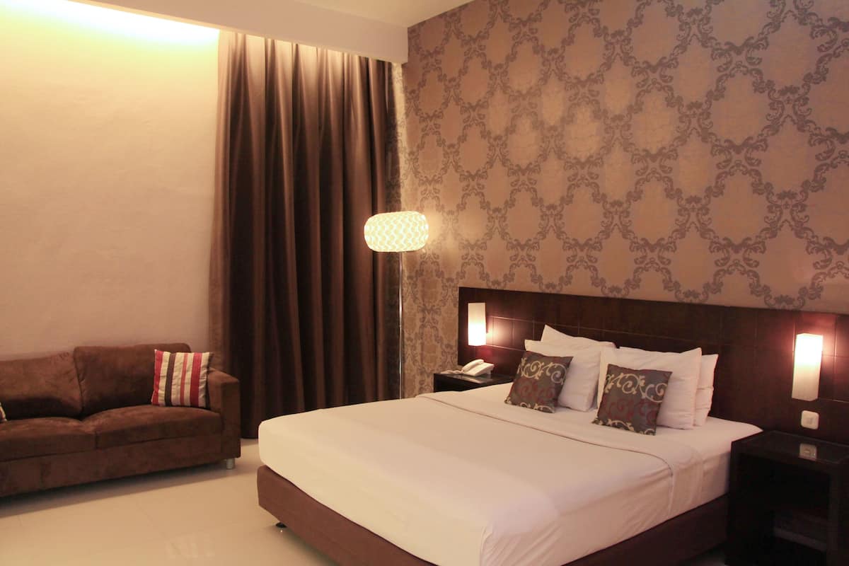 A hotel room with a large bed, a sofa, a nightstand with a lamp, and a patterned wallpaper.