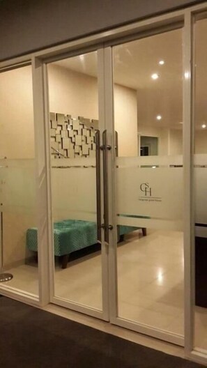 A hotel room with a sliding glass door, a bed with a green bedspread, a small table, and a wall with a geometric pattern. - Sisingamangaraja Guest House Semarang (Semarang)