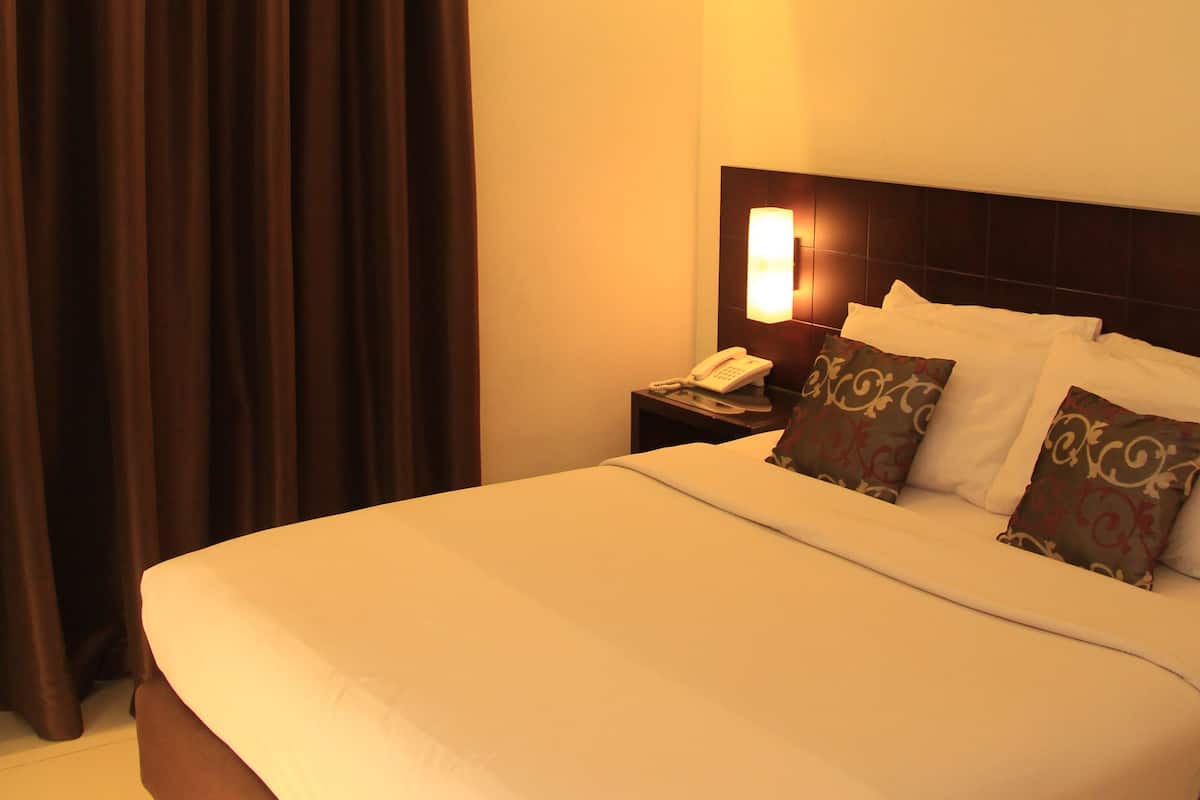 A hotel room with a large bed, a nightstand, a telephone, and a curtain.