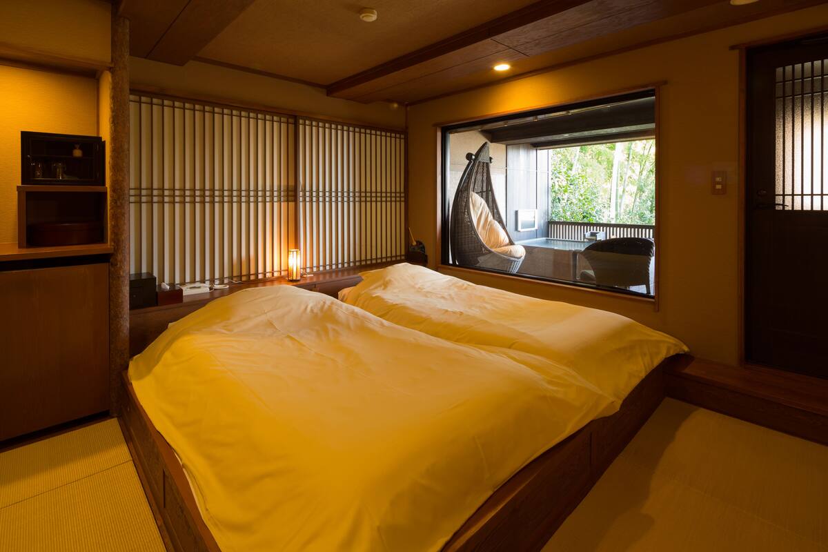 A room with a large bed, a window with a view of greenery, and a traditional Japanese sliding door.