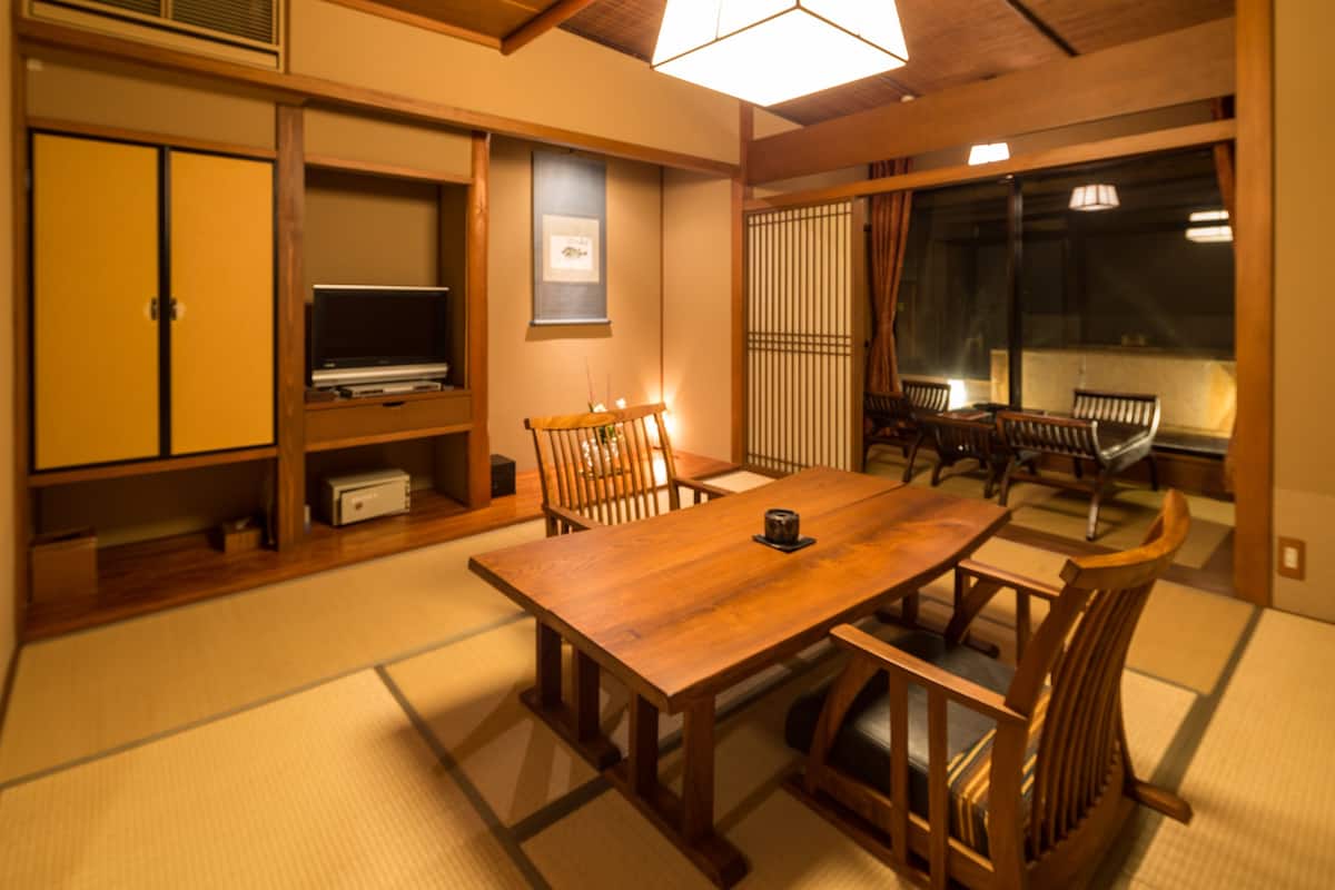 A traditional Japanese-style room with tatami flooring, a wooden dining table, and a television on a shelf.