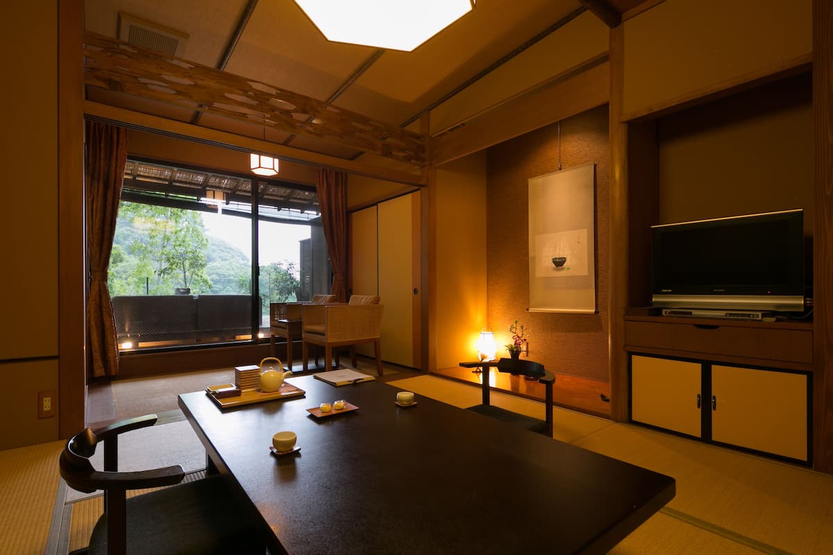 A traditional Japanese room with tatami flooring, a low table with tea set, a television, and a sliding door leading to a balcony.