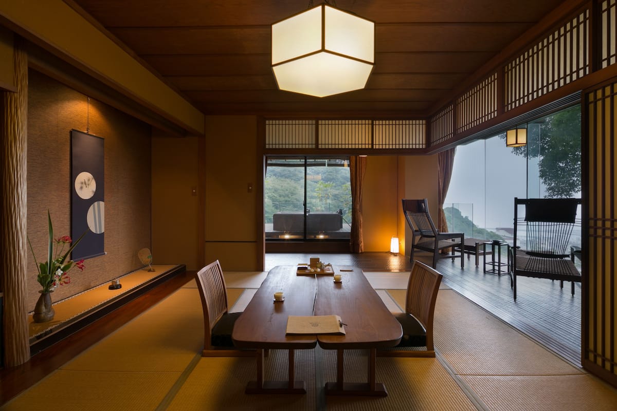 A traditional Japanese-style room with tatami flooring, a low table with cushions, and a view of the outdoors.