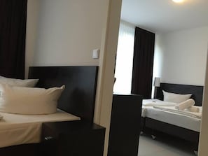 Una habitación de hotel con dos camas, una mesita de noche, una lámpara y una ventana con cortinas.