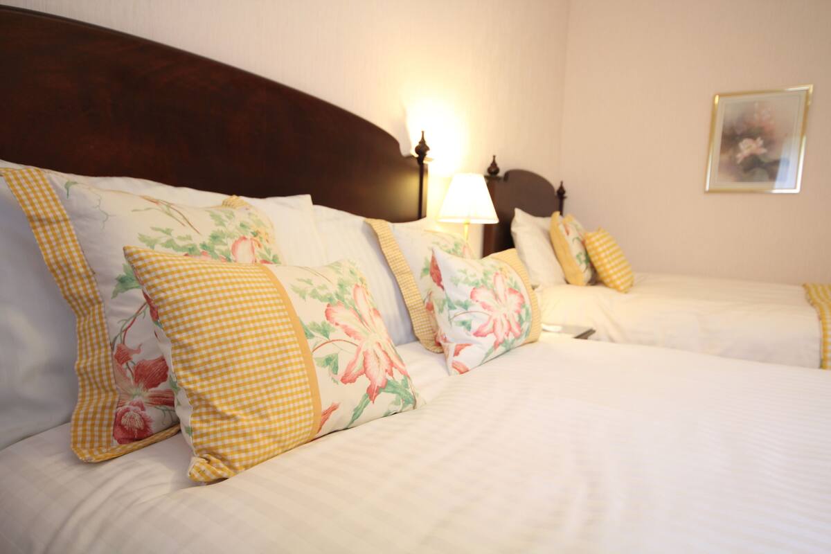 A hotel room with a wooden headboard, floral-patterned pillows, and a bedside lamp.
