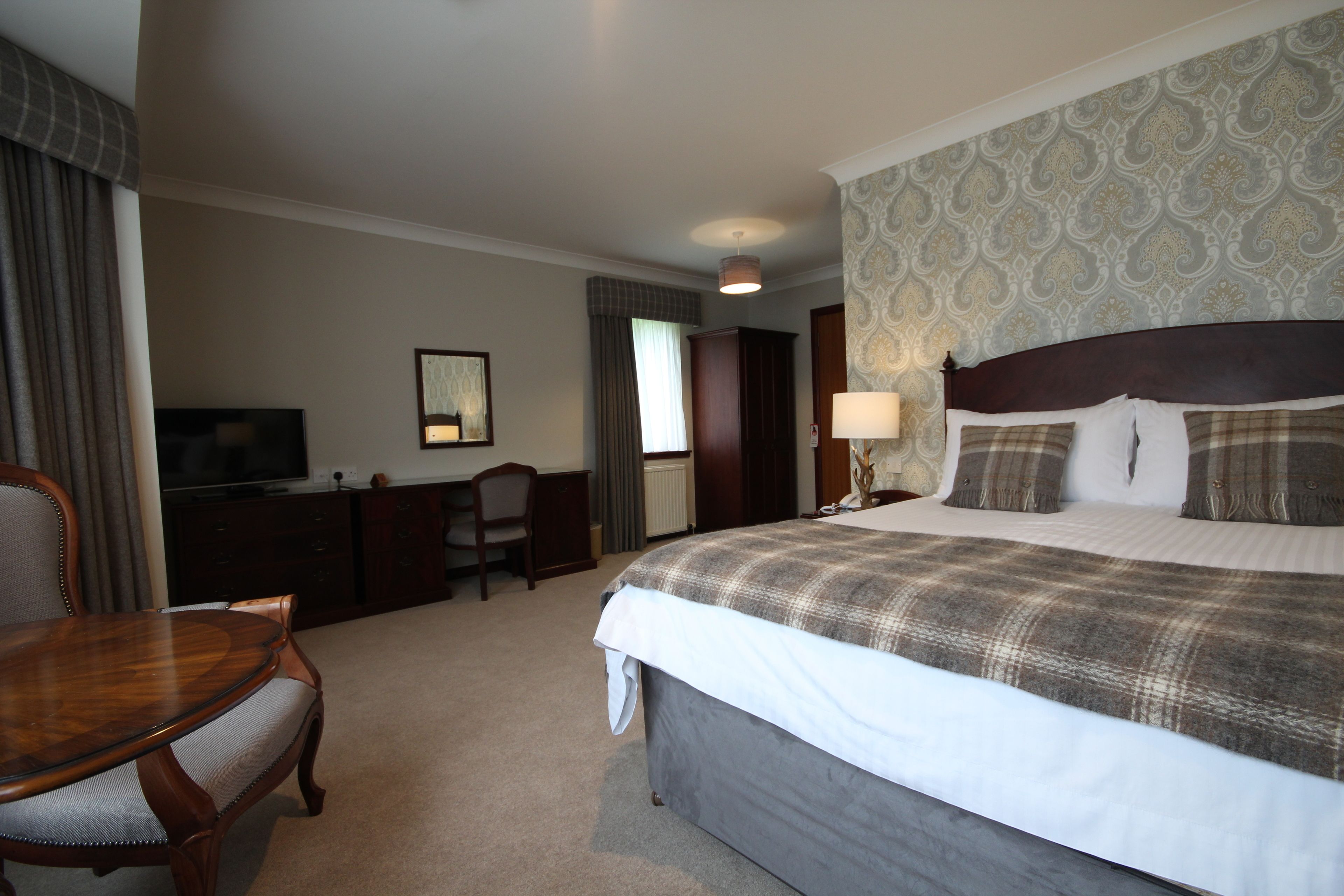 A hotel room with a large bed, a wooden desk, a television, and a chair.