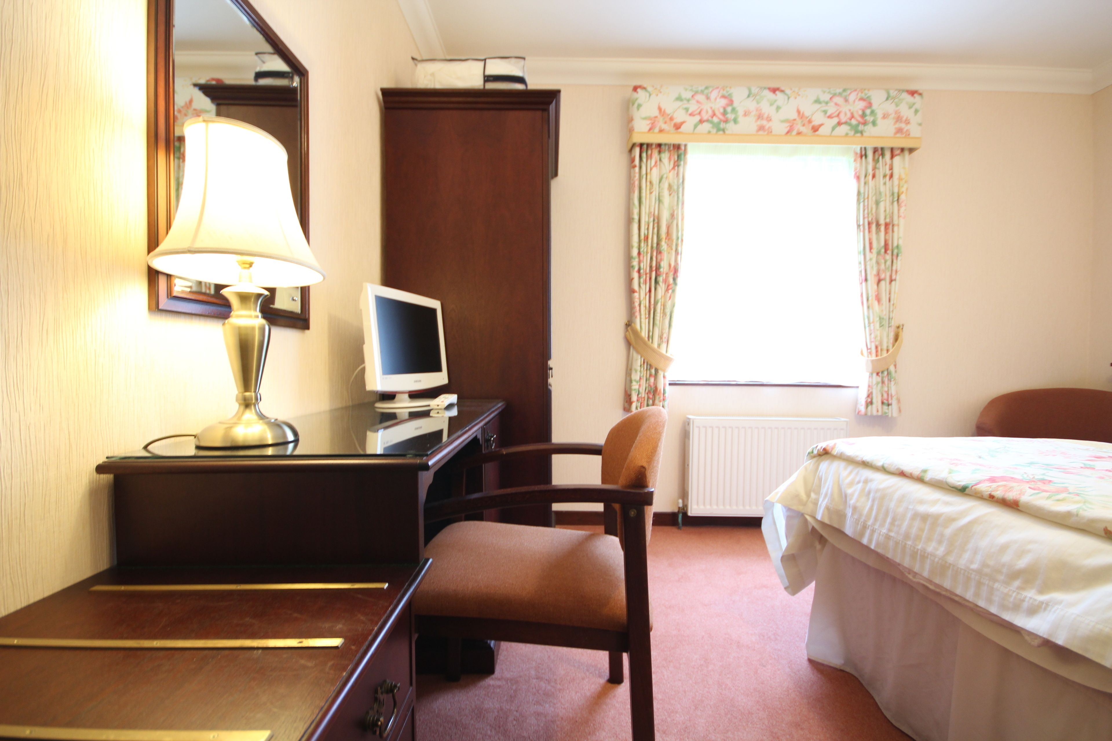 A hotel room with a desk, chair, bed, and a window with curtains.