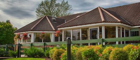 A two-story building with a tiled roof, a covered porch, and a green fence.