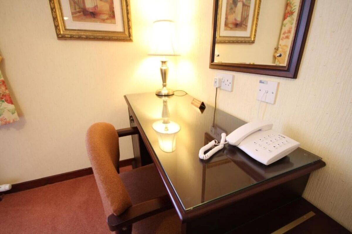 A hotel room with a desk, a telephone, a lamp, and a chair.