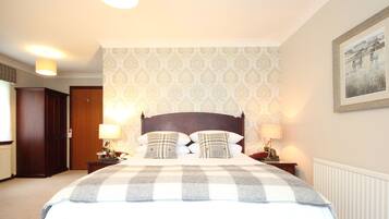 Een netjes ingerichte slaapkamer met een groot bed, twee nachtkastjes met lampen, een houten garderobe en behang met een patroon.