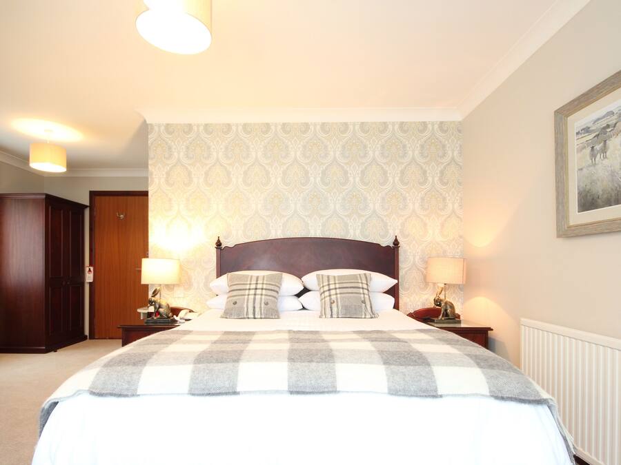 Een netjes ingerichte slaapkamer met een groot bed, twee nachtkastjes met lampen, een houten garderobe en behang met een patroon.