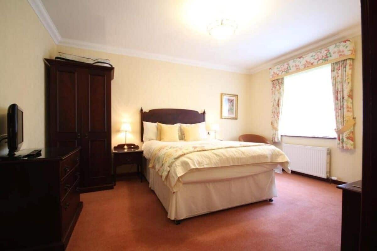 A bedroom with a bed, a nightstand, a dresser, a window with curtains, and a ceiling light.