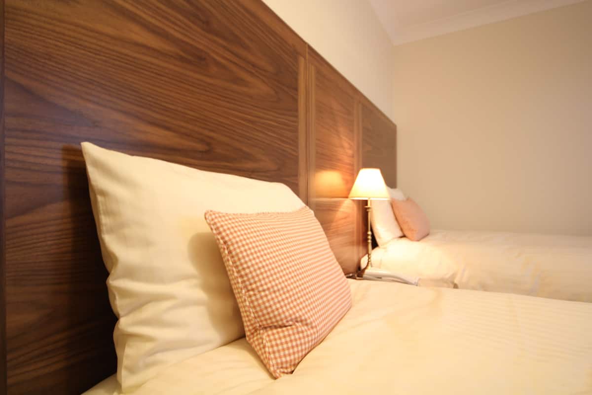 A hotel room with a wooden headboard, two beds, and a bedside lamp.