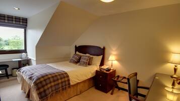 A bedroom with a bed, bedside table, lamp, chair, desk, and window.