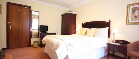 A hotel room with a bed, a television, a wardrobe, a desk, and a chair.