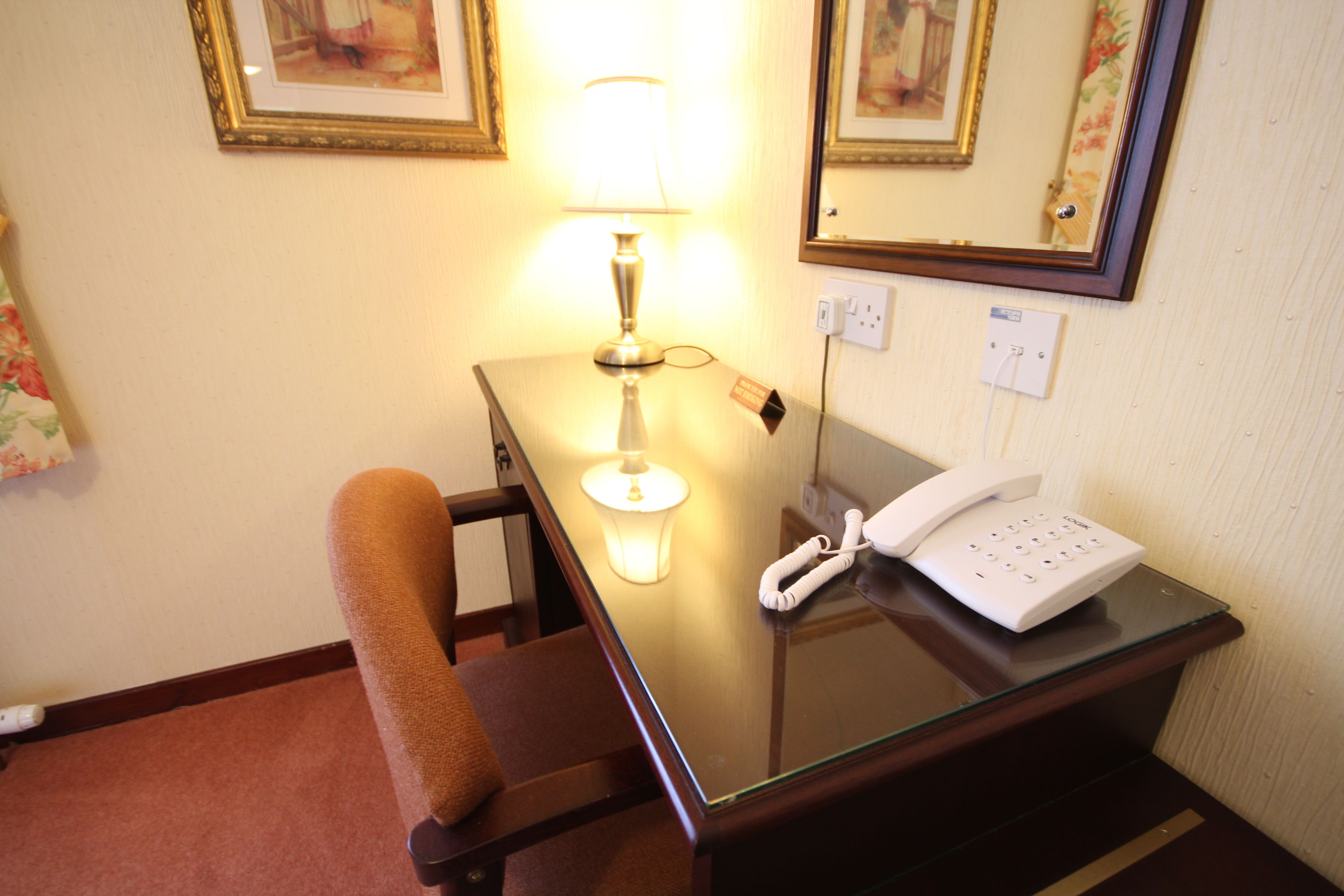 Una camera d'albergo con scrivania, sedia, lampada, telefono e specchio a parete.
