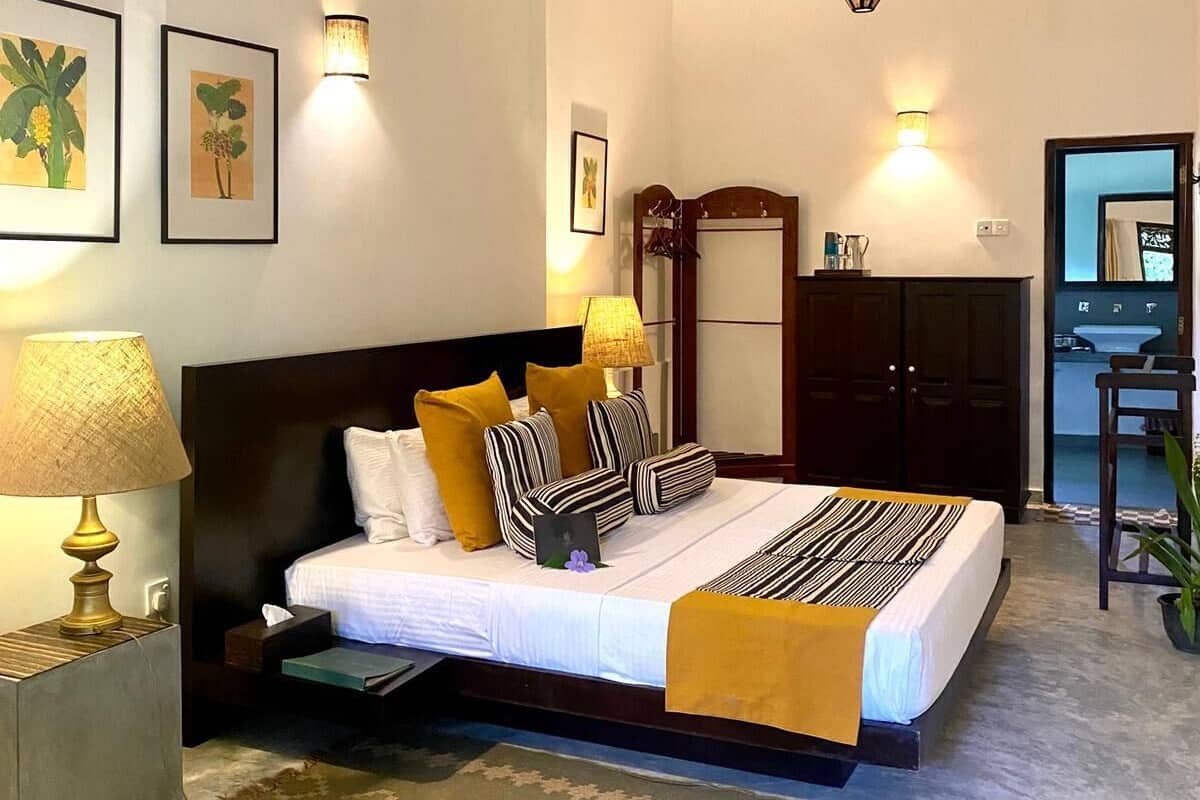 A hotel room with a bed, bedside lamps, a ceiling fan, a desk with a chair, and a view of the outside.