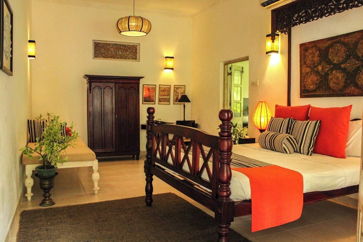 A bedroom with a wooden bed, a nightstand, a lamp, and a potted plant.