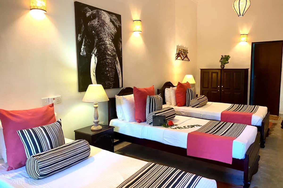 A hotel room with two beds, a nightstand, a lamp, a painting, and a door.