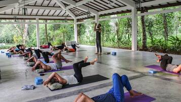 Un grupo de personas practicando yoga en un espacio al aire libre techado con vistas a exuberante vegetación.
