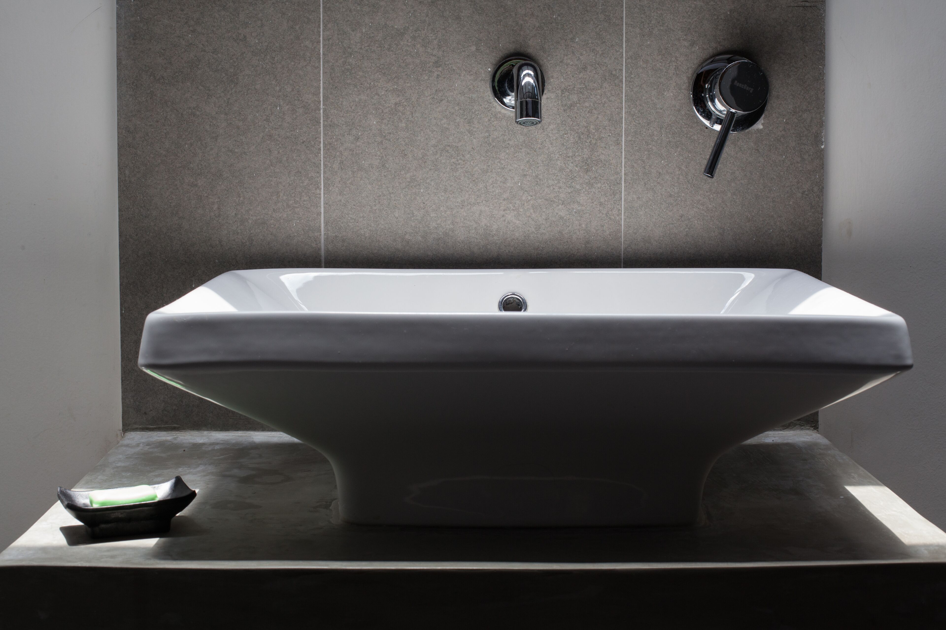 A modern bathroom with a rectangular sink, two faucets, and a soap dish.