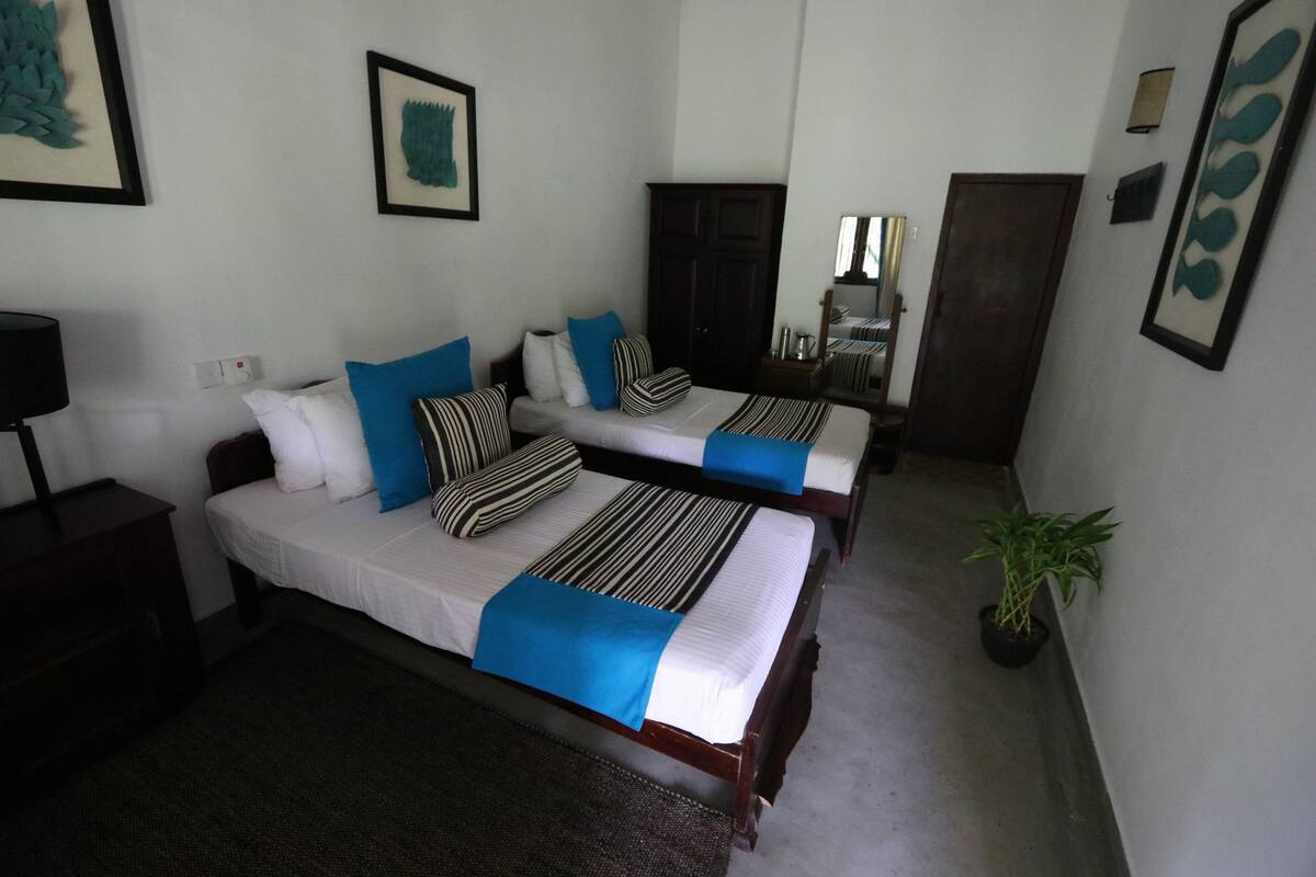 A hotel room with two beds, a dark wooden wardrobe, a small table, and a potted plant.