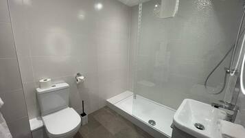 A modern bathroom with a toilet, a glass-enclosed shower, and a sink.