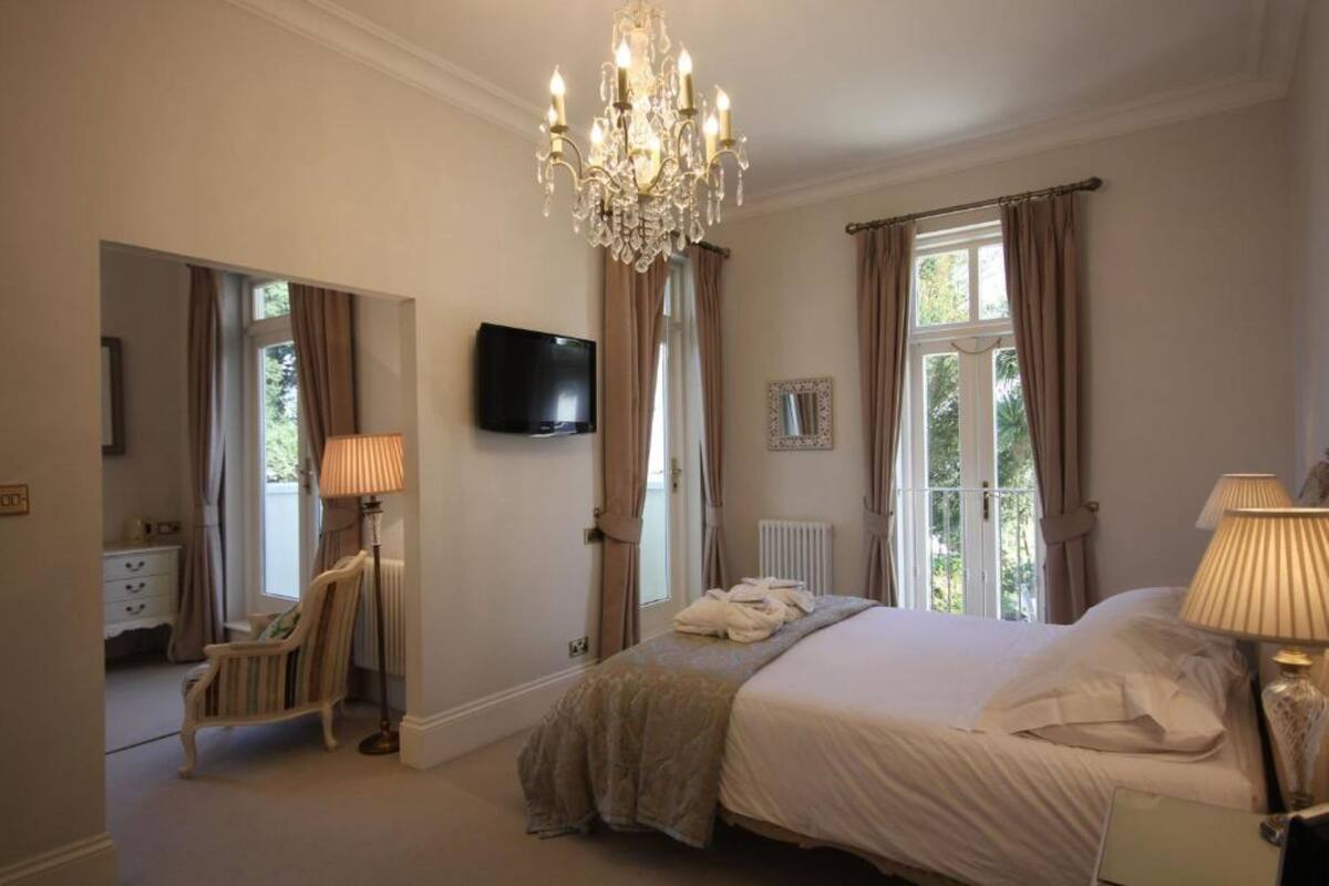 Quarto com cama grande, lustre, televisão e vista para o exterior.