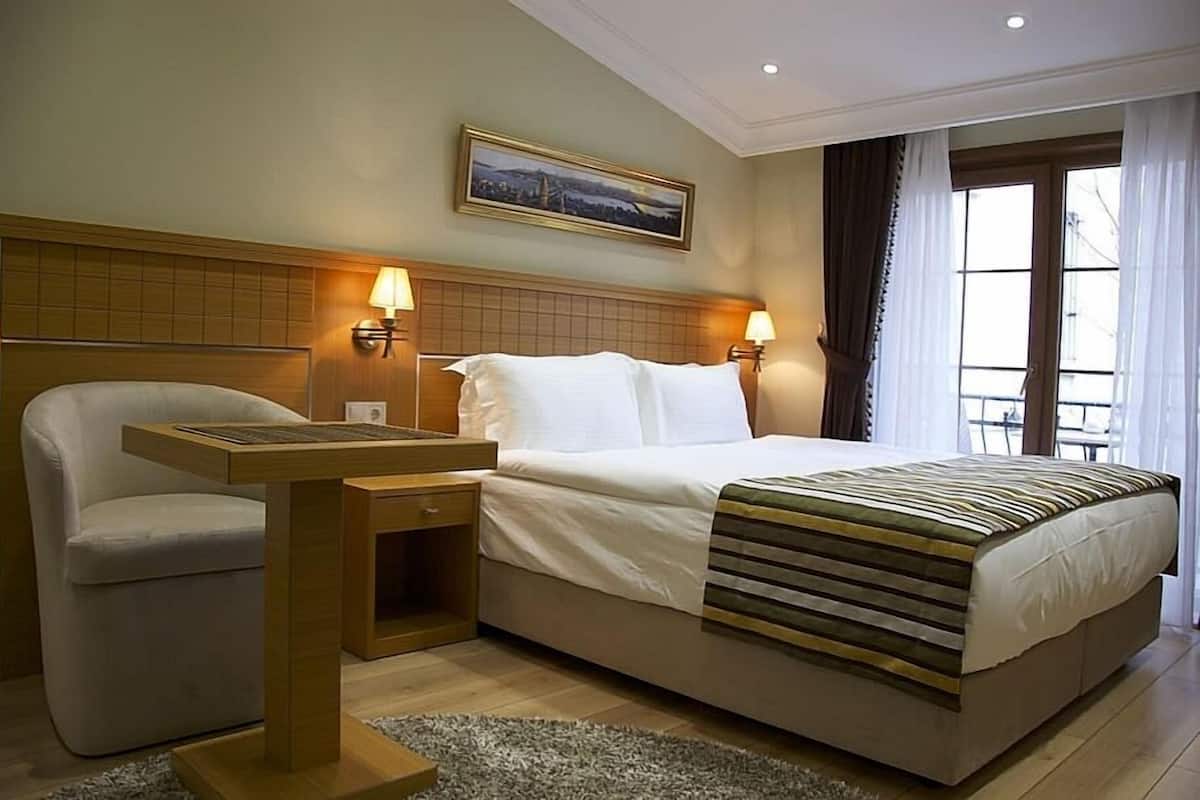 A hotel room with a bed, a chair, a desk, and two wall-mounted lamps.