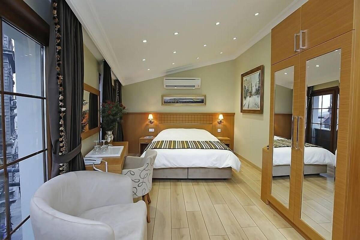 A hotel room with a large bed, a sitting area with a chair, a small table, and a mirror cabinet.