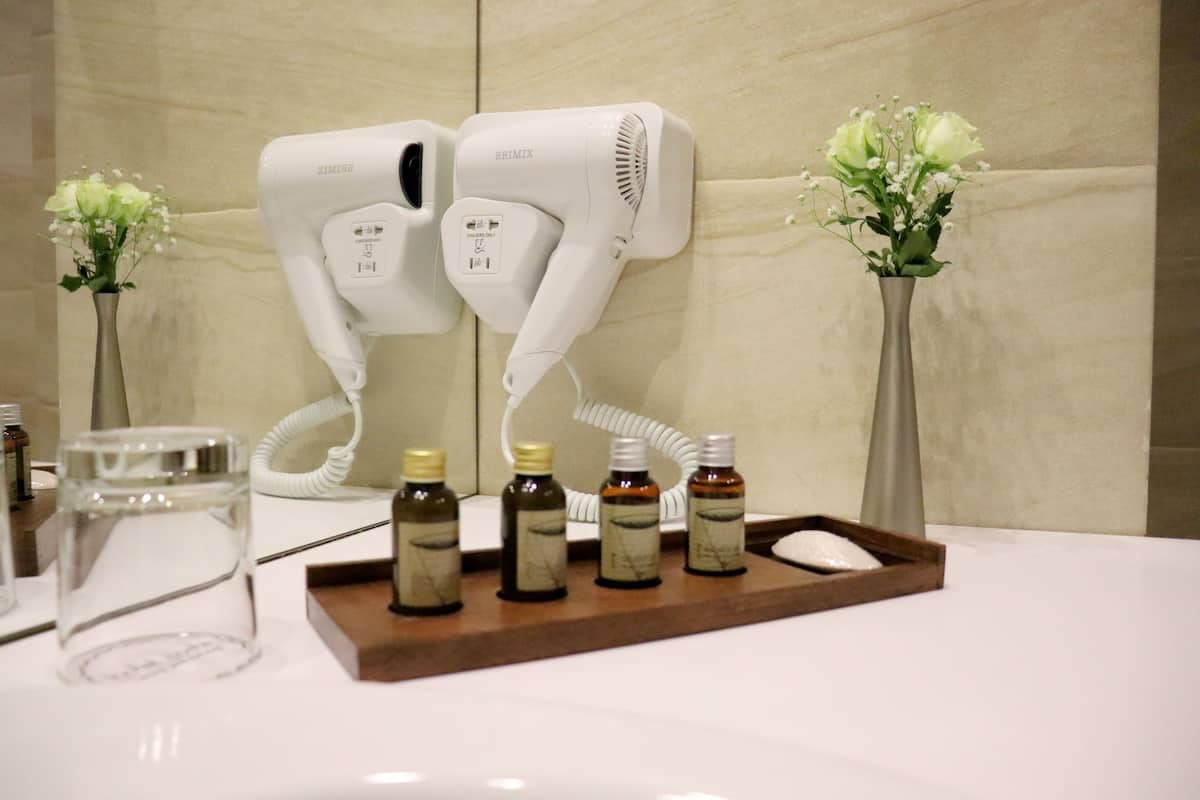 A bathroom with two hair dryers mounted on the wall, a tray with bottles, and two vases with flowers.