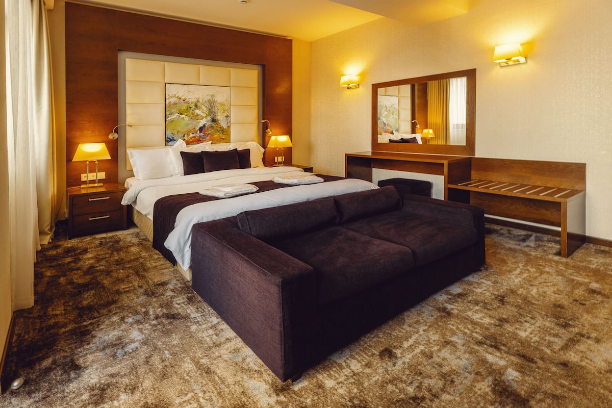 A hotel room with a large bed, a sofa, a desk, and a mirror.