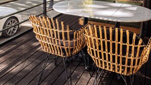 Et rundt bord med fletstole og en hængende lampe i et overdækket udendørs siddeområde.