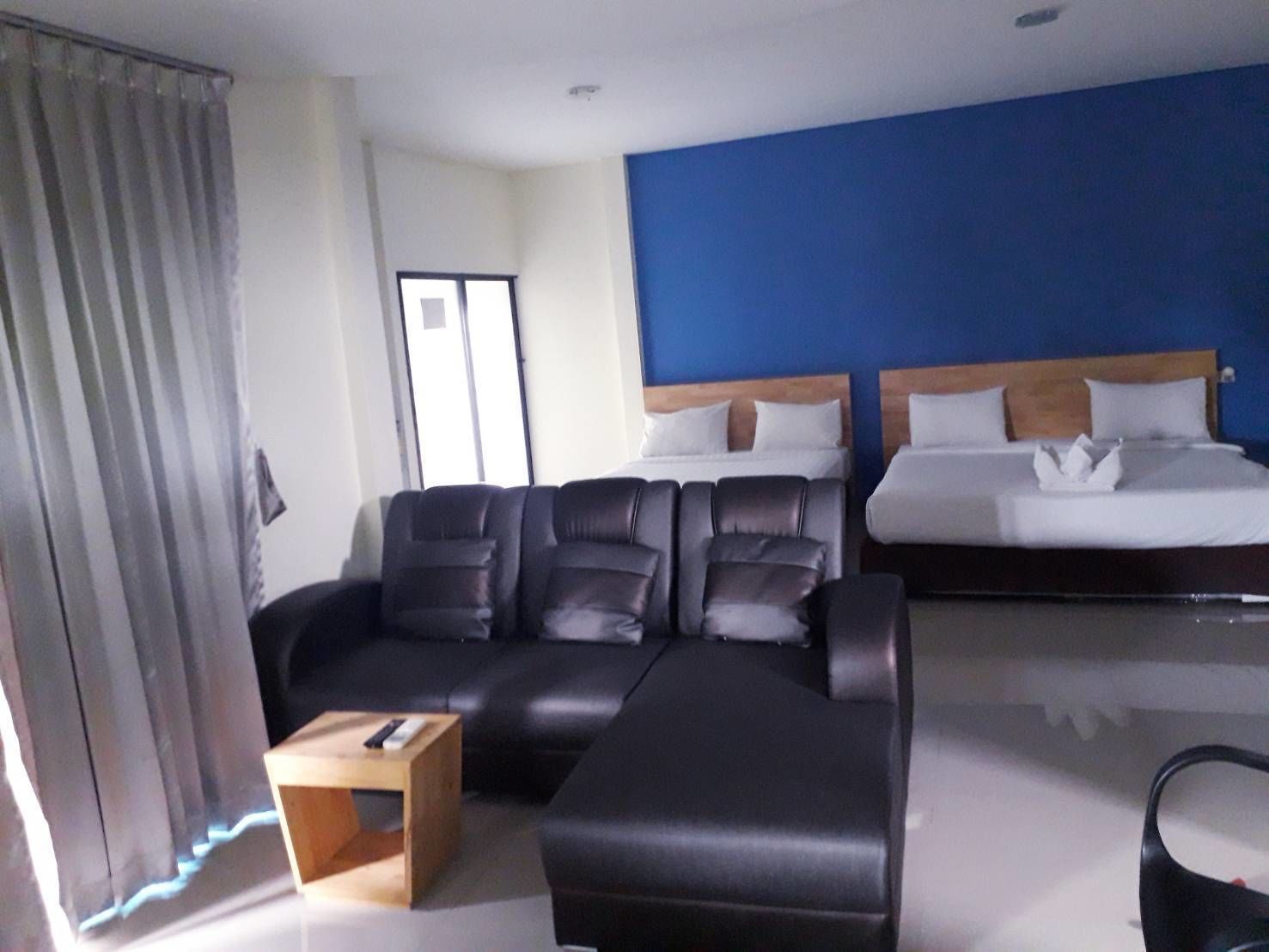 Habitación de hotel con sofá de cuero negro, una mesa de centro de madera, cama con ropa blanca y una pared de acento azul.
