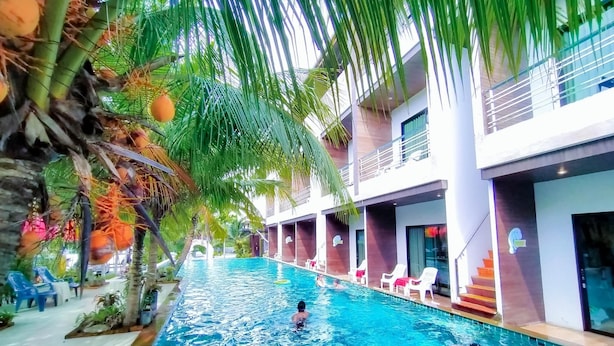 A swimming pool with a person in the water, surrounded by palm trees and modern buildings. - Rimnatee Resort Trang (Trang)