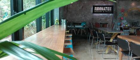 Un restaurant doté d’un long comptoir en bois, de chaises en métal et d’un mur en pierre sur lequel est affiché un panneau indiquant « RINNATEE RESORT @ TRANG ».