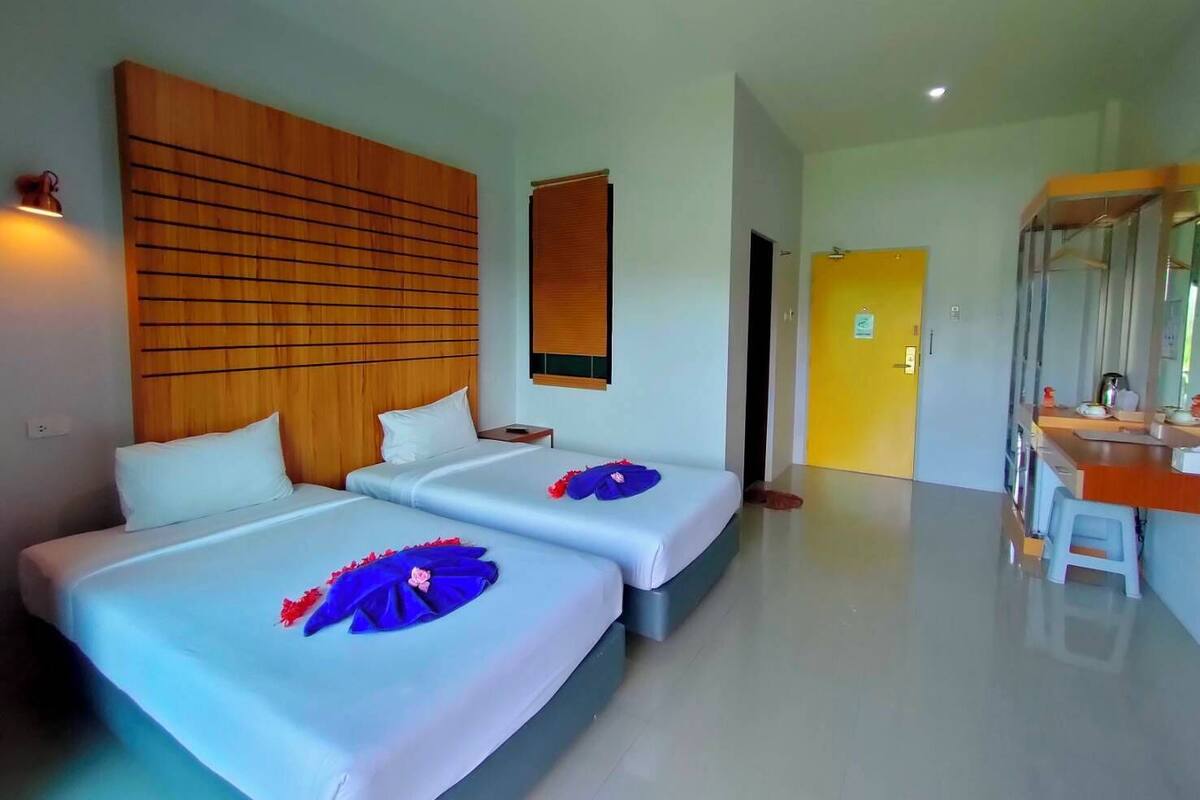A hotel room with two beds, a wooden headboard, a desk with a mirror, and a bathroom door.