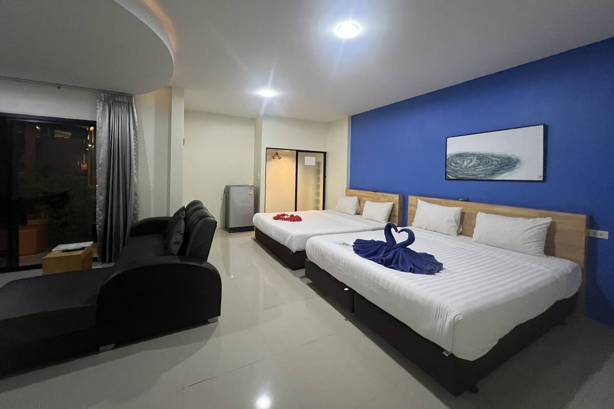 A hotel room with two beds, a sofa, a refrigerator, and a large window.