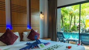 A hotel room with a bed, pillows, a decorative towel, and a view of a pool and palm trees. - Rimnatee Resort Trang (Trang)