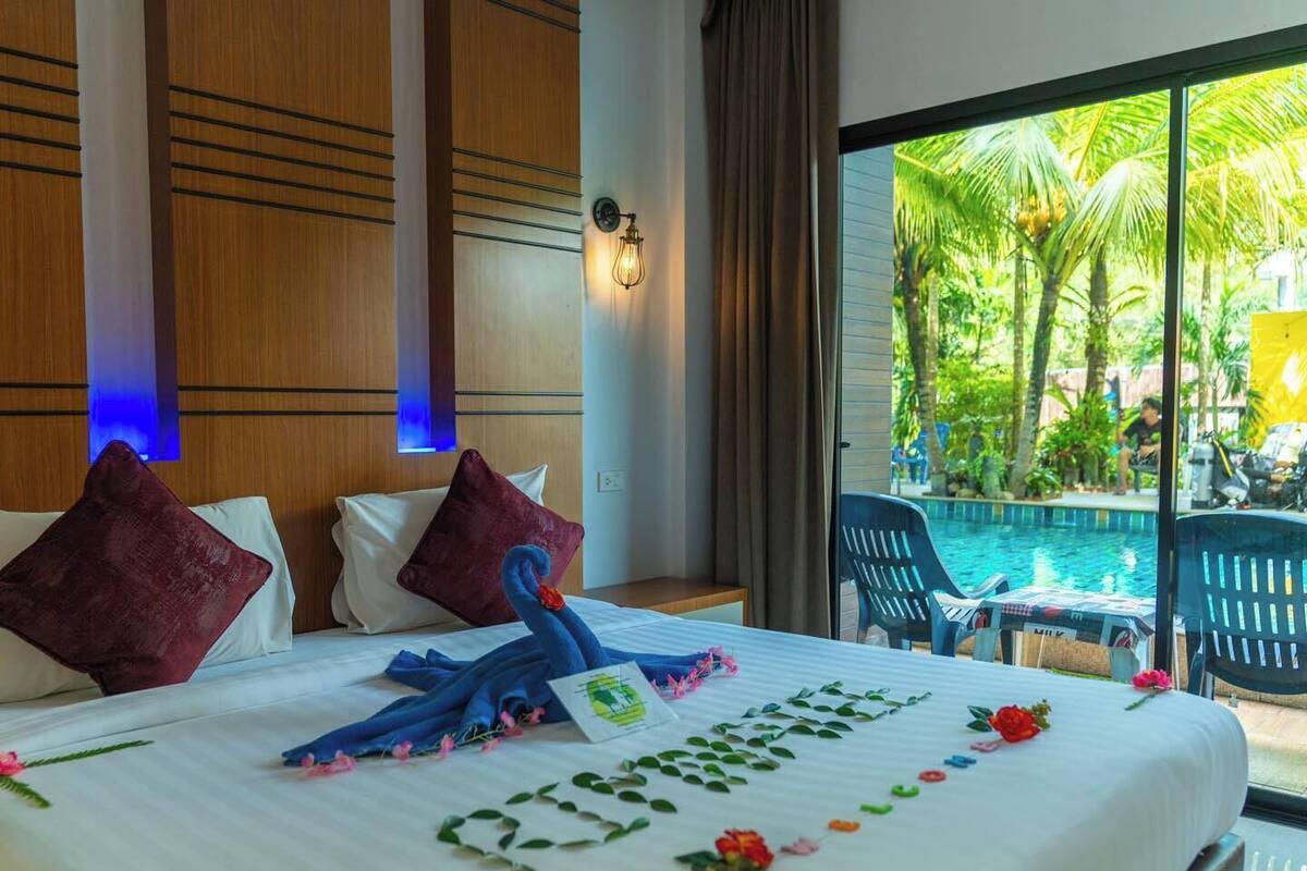 A hotel room with a bed, pillows, a decorative towel, and a view of a pool and palm trees.