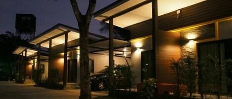 A modern building with a covered outdoor area, large windows, and a tree in the foreground.